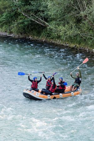 Raftinggruppe jubelt im Boot mit erhobenen Paddeln