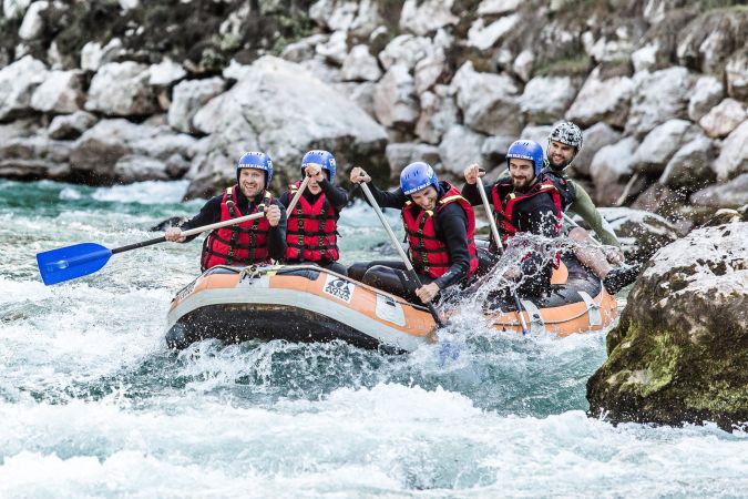 Raftingboot passiert eine hohe Welle neben einem Felsen auf der Saalach